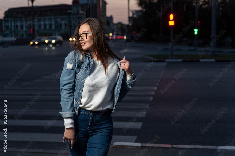 Brunette girl in youth clothes on evening city background. Stylish young woman in glasses on city street, summer time Brunette girl in youth clothes on evening city background. Stylish young woman in glasses on city street, summer time