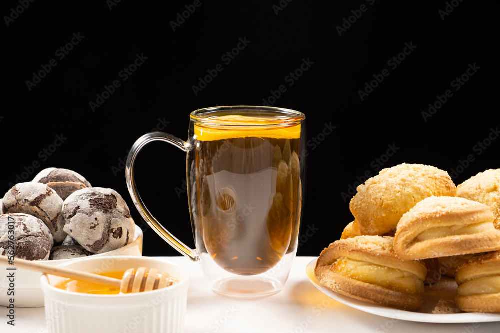 Tea with lemon and honey with cocoa cookies and cakes with creamy filling on a black background. Tea with lemon and honey with cocoa cookies and cakes with creamy filling on a black background.