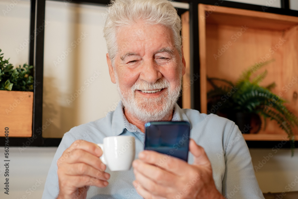 Handsome senior man sitting inside a cafeteria enjoying an espresso coffee cup while using mobile phone - caucasian elderly bearded man looking at smartphone Handsome senior man sitting inside a cafeteria enjoying an espresso coffee cup while using mobile phone - caucasian elderly bearded man looking at smartphone
