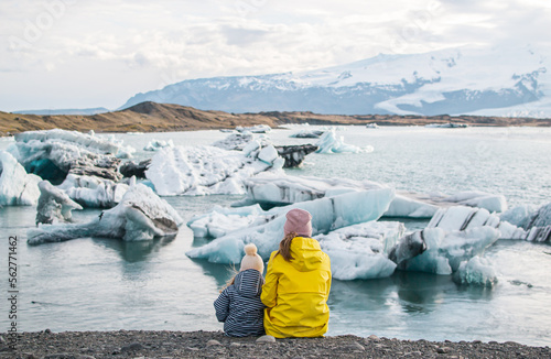 Mother with Daughter in Yellow Coat Walking on Glacial Lagoon in Iceland, Atlantic Ocean, Sunny Day