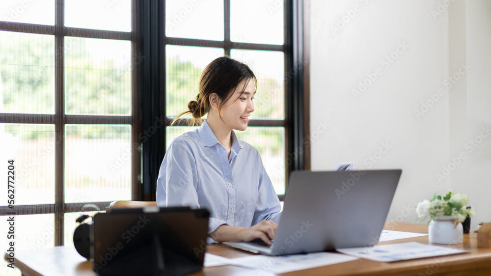 Woman using laptop to work or do homework at home with smiling face in her office, Creating happiness at work with a smile, Live performance or vdo call with laptop, Work from home. Woman using laptop to work or do homework at home with smiling face in her office, Creating happiness at work with a smile, Live performance or vdo call with laptop, Work from home.