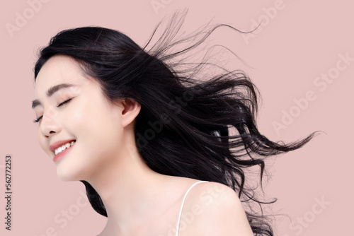 Beautiful Asian girl with long and shiny wavy hair isolated on pink background. Beautiful model with curly hairstyle and make up.