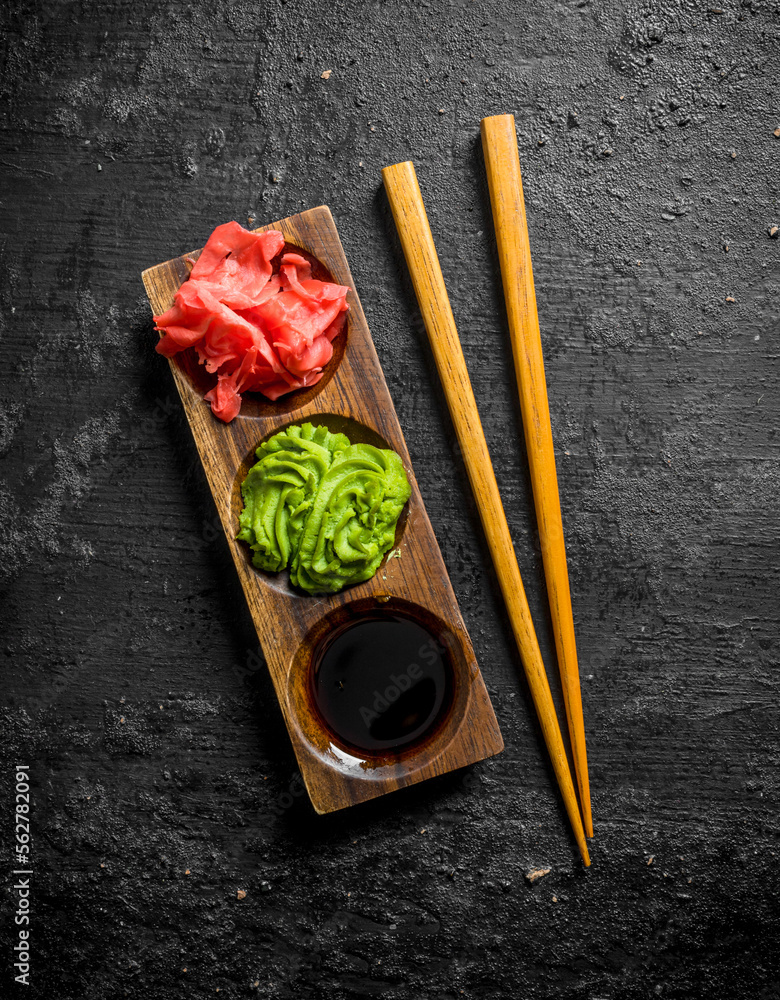 Wasabi, marinated ginger and soy sauce in a wooden stand with chopsticks.