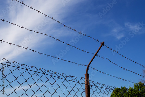 Barbed wire  triple wire  metal band with sharp spikes for fences. Rusty barbed wire against the blue sky. The concept of restricting rights and freedoms.
