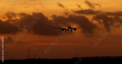 Silhouette of airplane lowers altitude and speed in preparation for landing on airport runway. Silhouette of passenger plane in orange sky. Long-awaited opening of borders after epidemic of covid-19