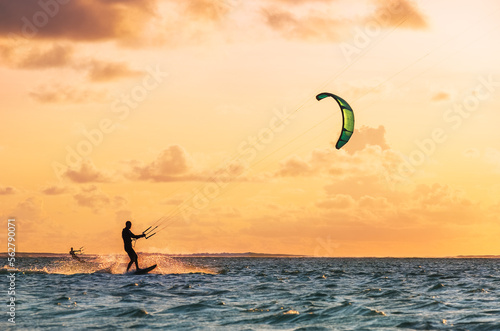 Sunset sky over the Indian Ocean bay with a two kiteboarders riding kiteboards with a green bright power kites. Active sport people and beauty in Nature concept image. Le Morne beach, Mauritius.