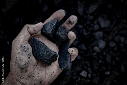 Hand holding coal. coal in a hand operations. Male hand with coal on the background of a heap of coal, copy space. Fossil fuels, environmental pollution. Concept industry mining.