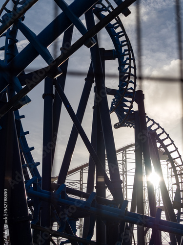twisting track of steel roller coaster ride strongly back light from low sunshine