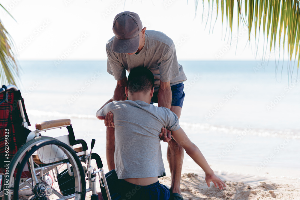 Fototapeta premium Father ​helping to carry young man with disability on the beach, Family activity on sea beach in summer,Lifestyle of disabilities boy and parent in travel holidays and nature therapy concept