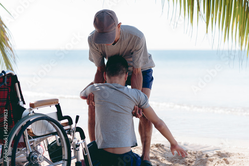 Father ​helping to carry young man with disability on the beach, Family activity on sea beach in summer,Lifestyle of disabilities boy and parent in travel holidays and nature therapy concept © GAYSORN