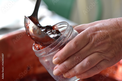 Zoom making strawberry jam horizontal photo, close up on hand put in jar. Shelf-stable cooking recipe fruit degustation
