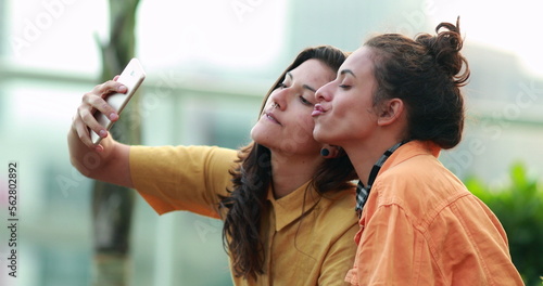 Candid authentic women using smartphone outside laughing reaction. Girls taking selfie with phone