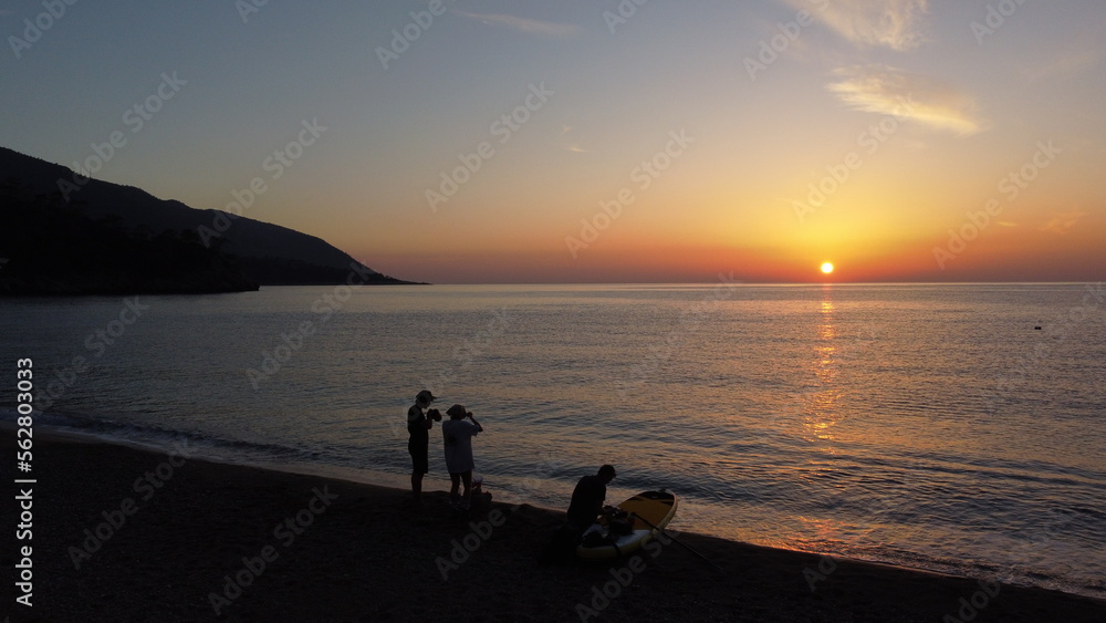 Three people on the beach meet the sunset