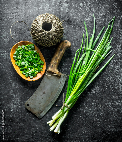 Bunch of green onion with chopped green onion on a plate  old knife and twine.