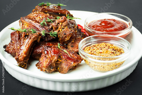 Baked ribs on a white plate. Roasted pork ribs with spices and herbs on a dark background. Food background. Side view. Copy space.