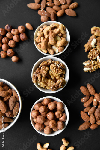 A set of nuts in white cups on a black background. Peanuts, hazelnuts and almonds. Walnut. A delicious set of nuts.