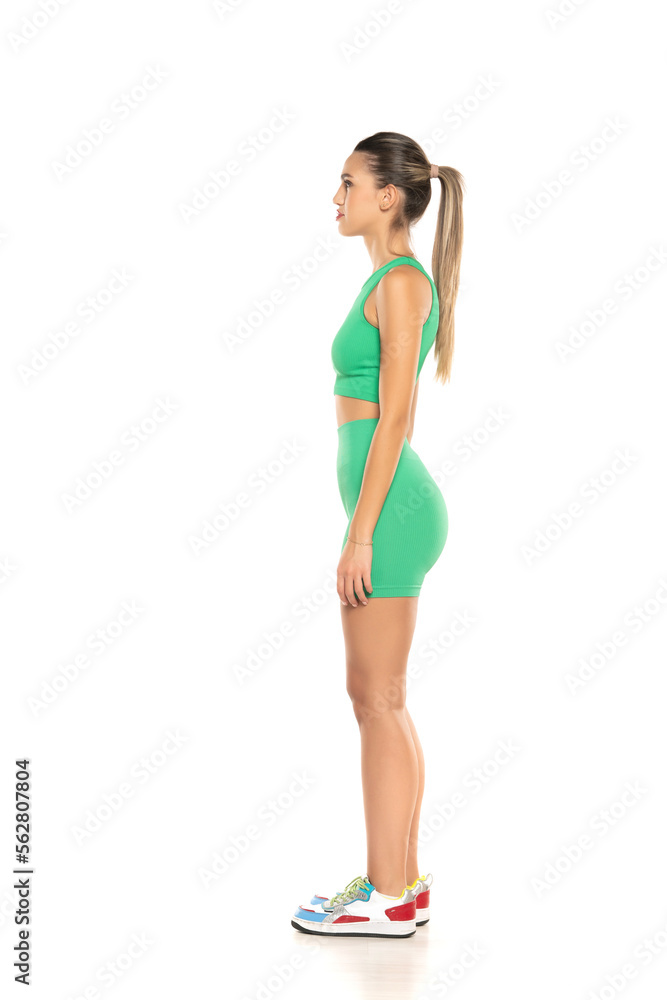 young sporty smiling woman in green shorts and top posing on white studio background. Side, profile view young sporty smiling woman in green shorts and top posing on white studio background. Side, profile view