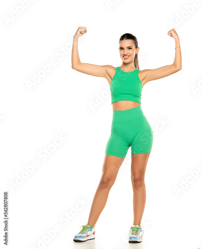 young sporty smiling woman in green shorts and top showing biceps on white background