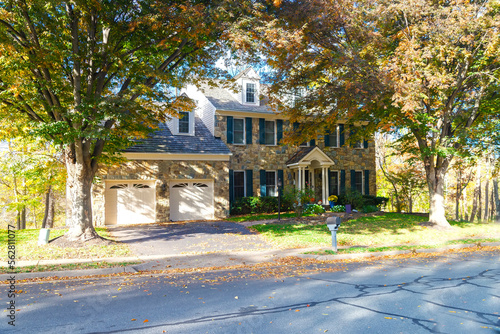 Large Suburban Brick House with Garage and Fall Holiday Decorations. Trimmed lawn and autumn leave on green grass.