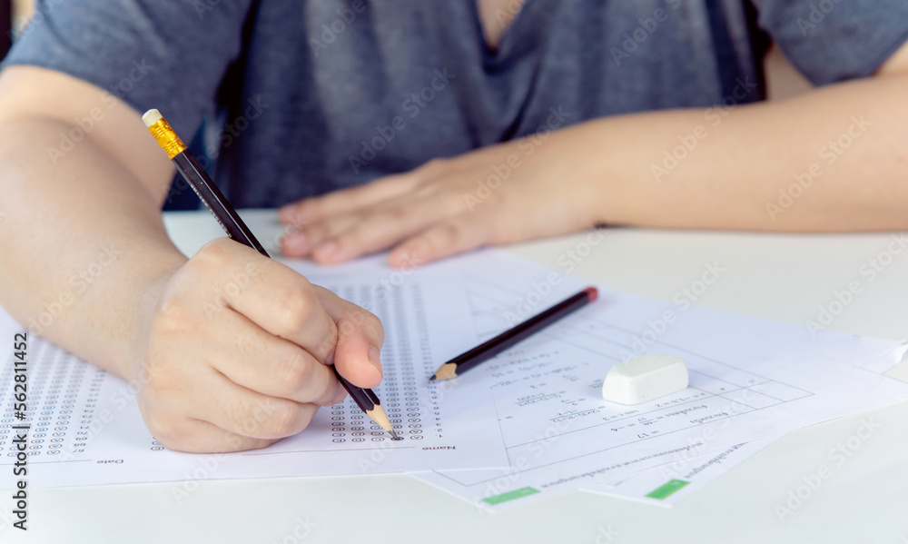 Students hand holding pencil writing selected choice on answer sheets and Mathematics question sheets. students testing doing examination. school exam