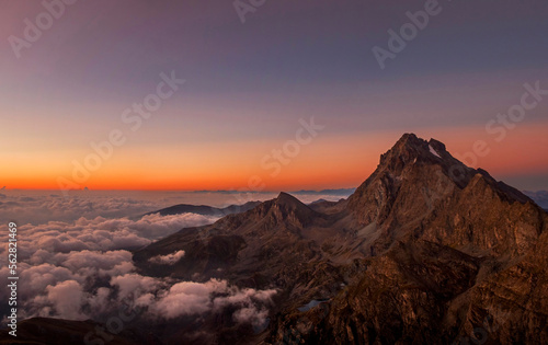 Enchanting view of the Western Alps at dawn with Monviso (3841 m) standing out against the colorful horizon and the clouds downstream that wrap it like a blanket. Monviso Park. August