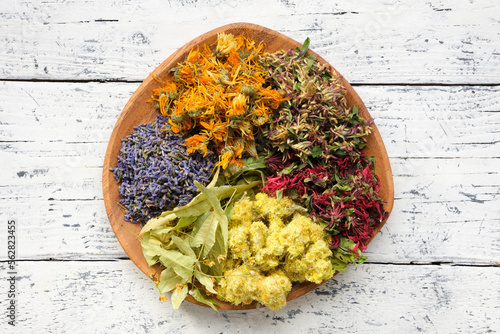 Wooden plate of medicinal herbs - lavender, calendula, red clover, helichrysum, lime tree flowers - ingredients for making of herbal medicine drugs, tea or infusion. Alternative herbal medicine. photo
