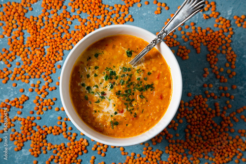 Top view of a bowl of red lentil soup surrounded by uncooked lentils photo