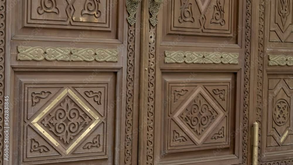 Large wooden entrance door to the mosque, decorated with beautiful patterns and Arabic script, beautifully carved wood and brass handles. Shot in motion Large wooden entrance door to the mosque, decorated with beautiful patterns and Arabic script, beautifully carved wood and brass handles. Shot in motion