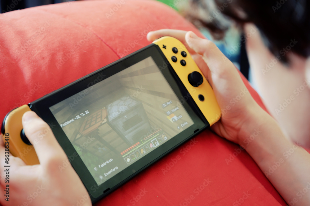 Obraz premium BARI, ITALY - OCTOBER 2, 2022: a kid playing with the Nintendo Switch gaming console, checking an inviting mysterious treasure chest. Handheld closeup shot.