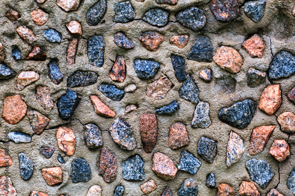 Textured concrete wall interspersed with multi-colored and variously shaped stones.