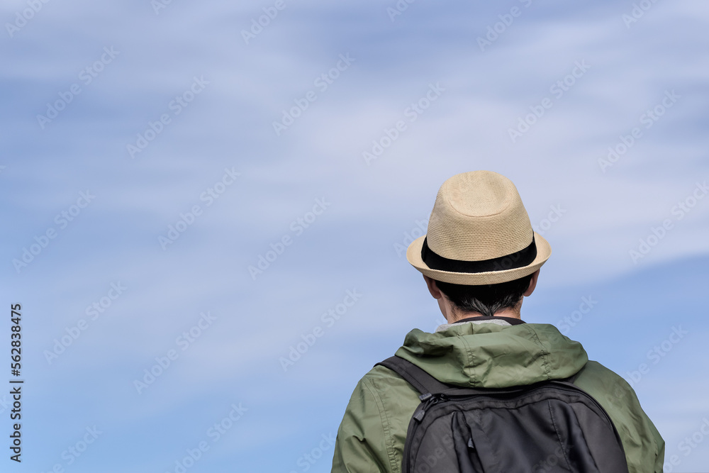 Back view of a traveler man with a backpack against the blue sky. Tourist, backpacker in a hat looks at the sky. Back view of a traveler man with a backpack against the blue sky. Tourist, backpacker in a hat looks at the sky.