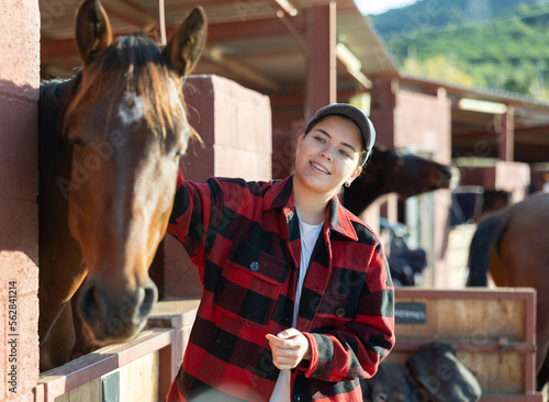 Caring young female farmworker petting stroking head of horse on animal ranch club on autumn sunny day