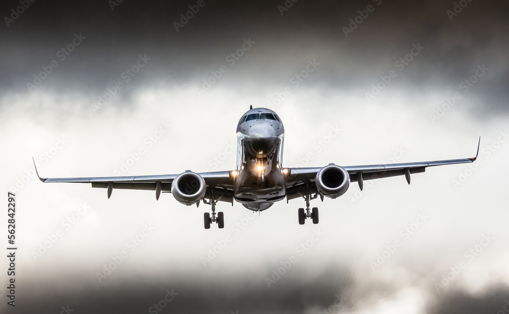 Between dark clouds, front view of a plane during the approach phase, about to land. 