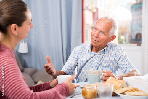 Elderly father and adult daughter talk and drink tea in the kitchen. High quality photo