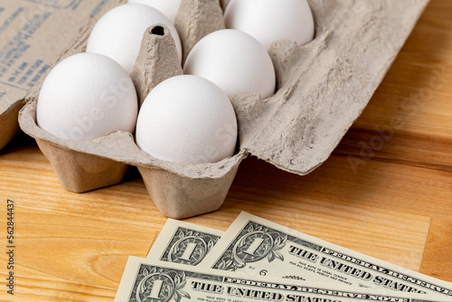 Fresh white chicken eggs in carton with cash money. Egg price, grocery shopping and poultry farming concept. 