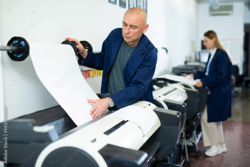 Obraz premium Service man uses plotter and checks the functionality in printing shop