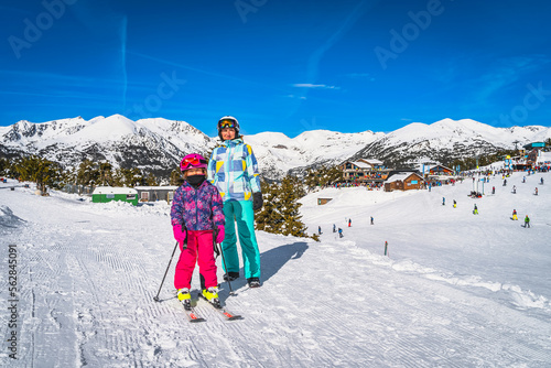 Mother and daughter, family, on ski, standing and smiling, ski resort, snow capped mountains and forest in background. Winter holidays, Andorra
