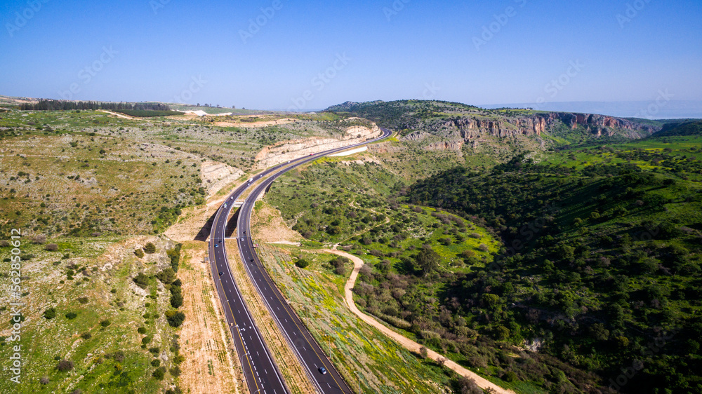 Aerial view shot flying over green hills fields, presents highway road and modern bridge with driving cars. curvy road through green mountains