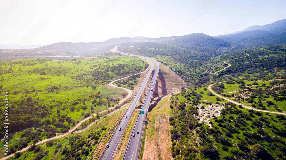 Aerial view shot flying over green hills fields, presents highway road and modern bridge with driving cars. curvy road through green mountains