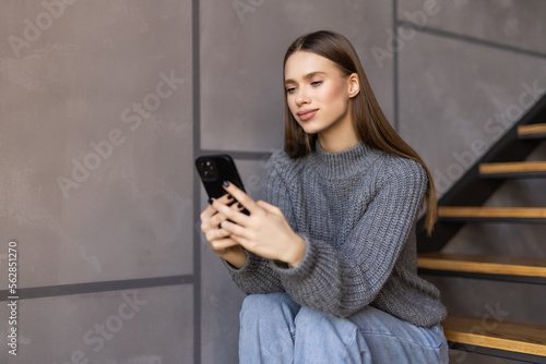 Attractive young woman sitting on the stairs and using her cellphone while home alone