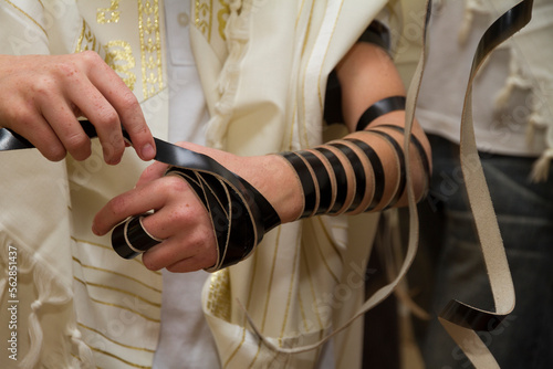 An young man wrapping Jewish Tefillin on his arm and wearing prayer shawl for praying. Preparing for a pray