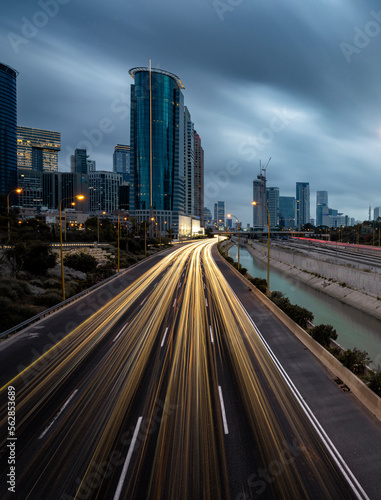 Night shot of cars tail lights at ayalon highway, with tel aviv skyline, urban skyscrapers and beautiful moving clouds, Israel