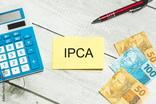A sigla IPCA referente ao Índice Nacional de Preços ao Consumidor Amplo escrita em um pedaço de papel. Notas do Real Brasileiro na composição. Economia brasileira. photo