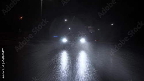 The car is driving at night in heavy rain on an asphalt road at high speed. Headlights shine through the rain. A beam of light from the headlightsView of the car in front of the bumper