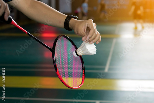 Badminton player is holding white badminton shuttlecock and badminton racket in front of the net before serving it over the net to another side of court.  © Sophon_Nawit