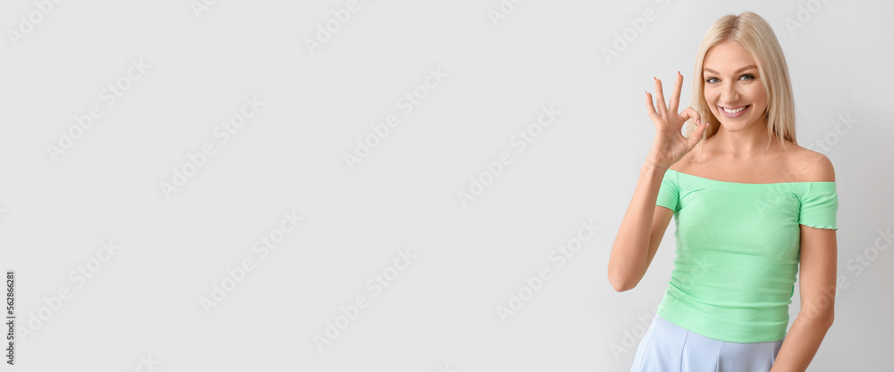 Beautiful smiling young woman showing OK gesture on light background with space for text Beautiful smiling young woman showing OK gesture on light background with space for text