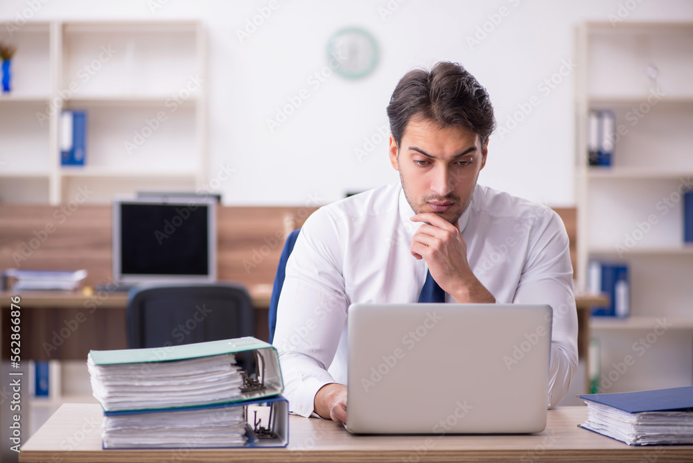 Young male employee unhappy with excessive work in the office Young male employee unhappy with excessive work in the office