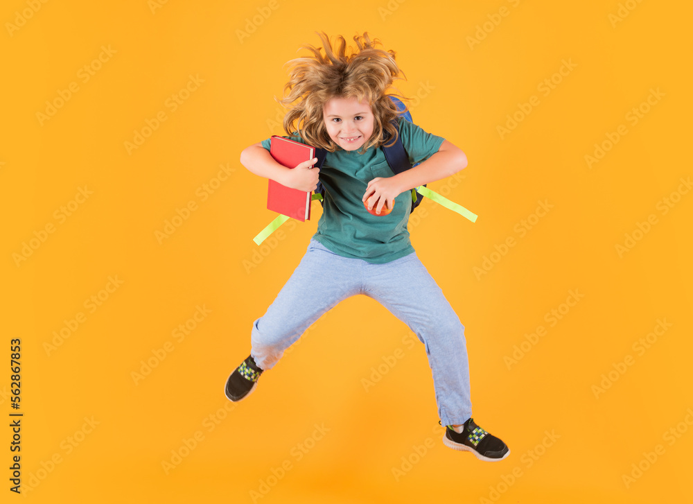 Full length of excited kid jumping. School boy in school uniform with backpack jumping on yellow isolated background. Kids learning knowledge and kids education concept.