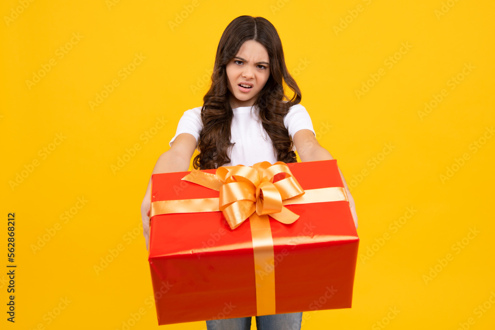 Unhappy sad teenager girl. Teenage child holding gift box on yellow isolated background. Gift for kids birthday. Christmas or New Year present box. Unhappy sad teenager girl. Teenage child holding gift box on yellow isolated background. Gift for kids birthday. Christmas or New Year present box.