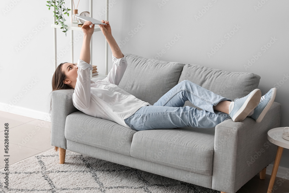 Young woman with tablet computer lying on sofa at home Young woman with tablet computer lying on sofa at home